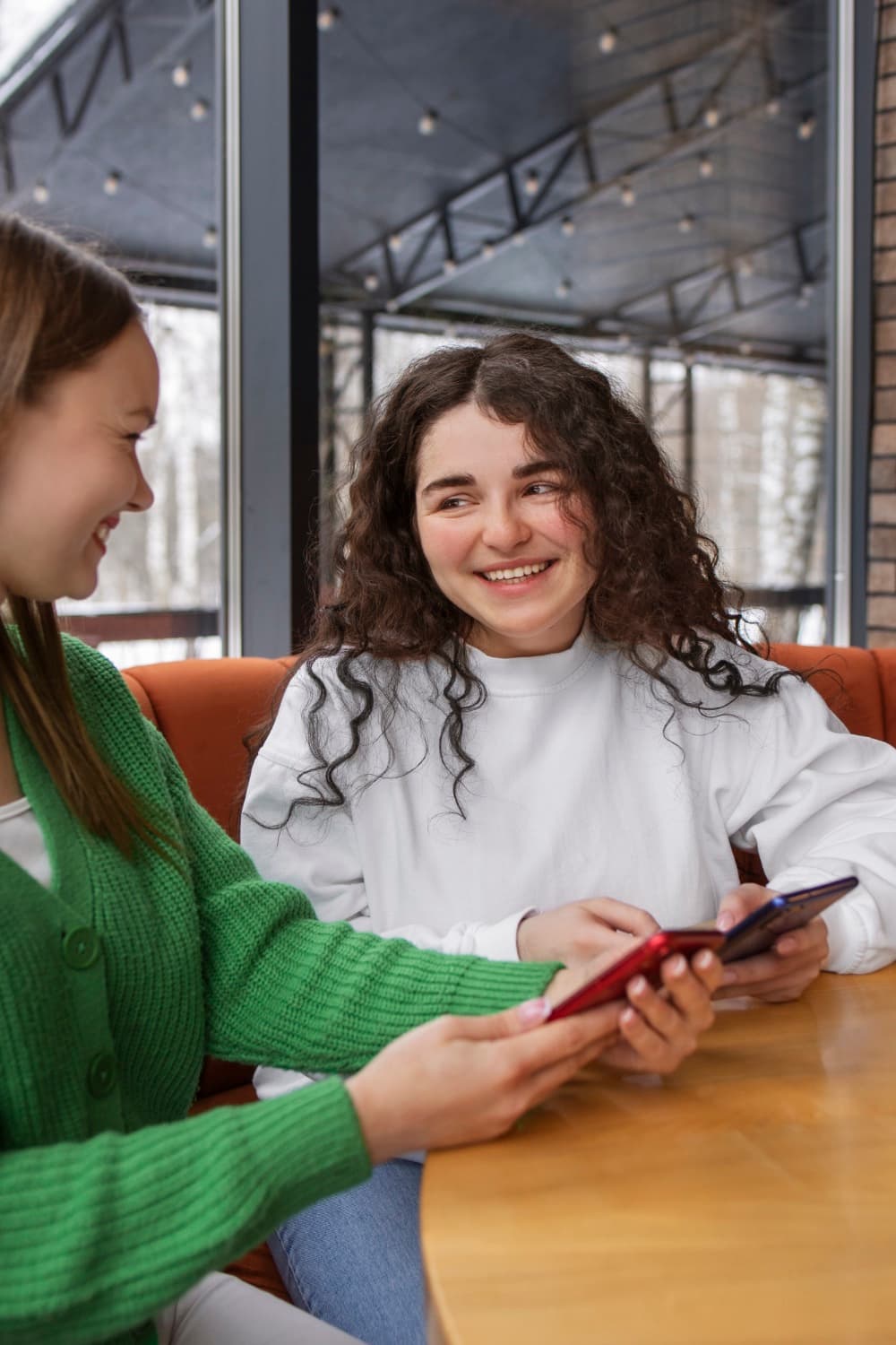 Zwei junge Frauen sitzen lächelnd zusammen und schauen auf ihre Smartphones - Symbol für moderne Kommunikation und Verbindung